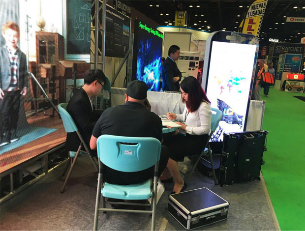 奥兰多橘城会展中心酷游九州展位现场，外贸部经理黄勇强和何巧玲与意向客户在交谈中